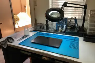 Reassembled Android tablet on a workbench with precision tools and a magnifying lamp in a Phoenix, AZ workshop.