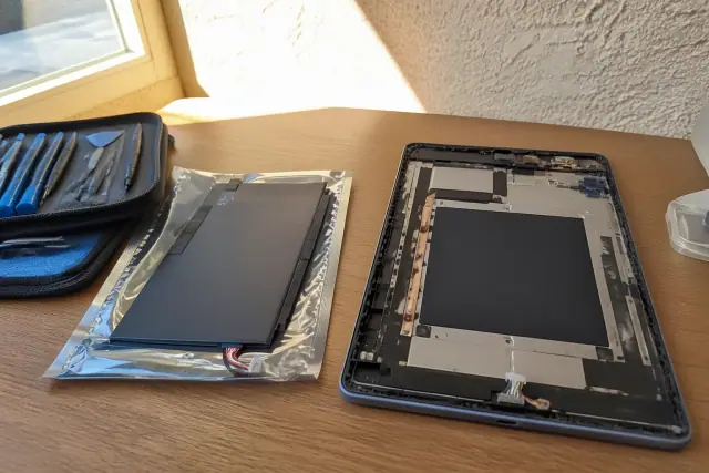 Replacement battery and open tablet chassis on a workbench in a Phoenix, AZ workshop.