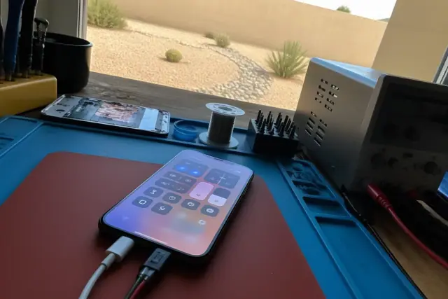 Smartphone connected to diagnostic cables on a testing bench during battery repair in Phoenix, AZ.