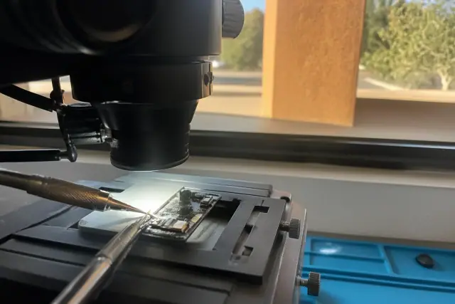 Close-up of a soldering iron repairing a logic board under a microscope in a Phoenix, AZ workshop.