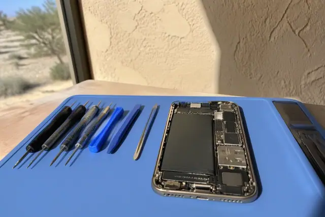 Smartphone with exposed internal components and repair tools on a workstation in Phoenix, AZ.