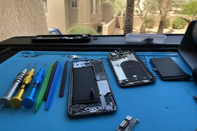 An open smartphone undergoing charging port repair on a workbench in Glendale, AZ.