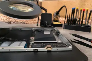 Smartphone with a repaired charging port under a magnifying lamp at a workbench in Phoenix, AZ.