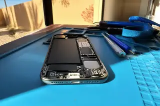 Smartphone with a new charging port on an anti-static mat with tools in a Phoenix, AZ workshop.