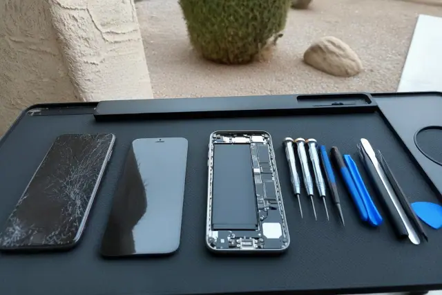 Smartphone with a cracked screen and exposed internal components at a workstation in Phoenix, AZ.
