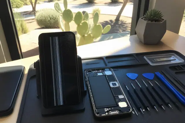 Shattered smartphone screen with display lines and internal components on a workstation in Phoenix, AZ.