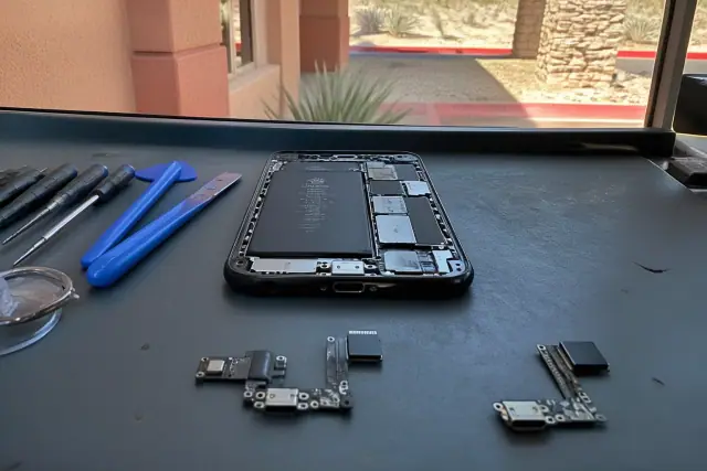 Smartphone repair technician comparing a flex-cable and soldered charging port on a logic board in Phoenix, AZ.