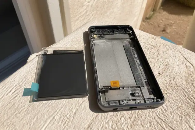 Smartphone replacement battery kit next to an open phone chassis on a sunlit stucco surface in Phoenix, AZ.