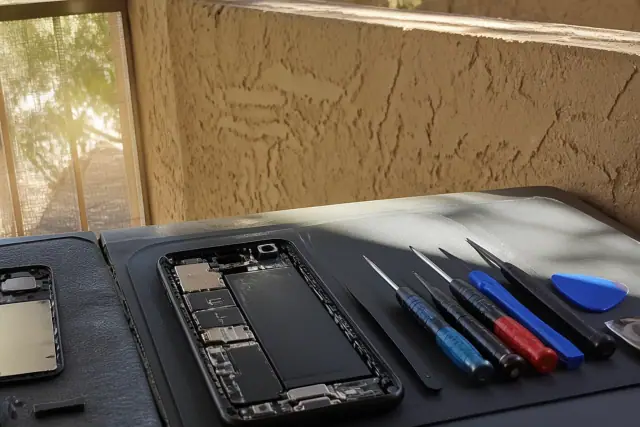 Opened smartphone with internal components and repair tools on a workstation in Phoenix, AZ.