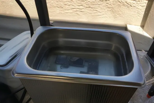 A circuit board submerged in an ultrasonic cleaning bath for water damage repair in Phoenix, AZ.