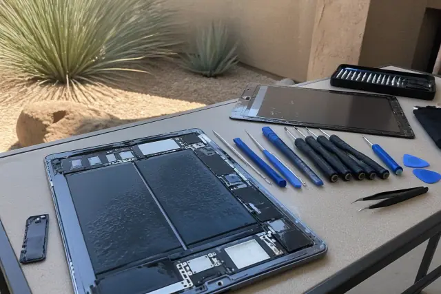 Open tablet and smartphone on a repair workbench with tools in Phoenix, AZ, set against a desert stucco exterior.