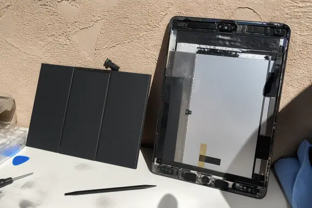 An open device and new battery on a messy workbench in Phoenix, AZ, with a stucco wall in the background.