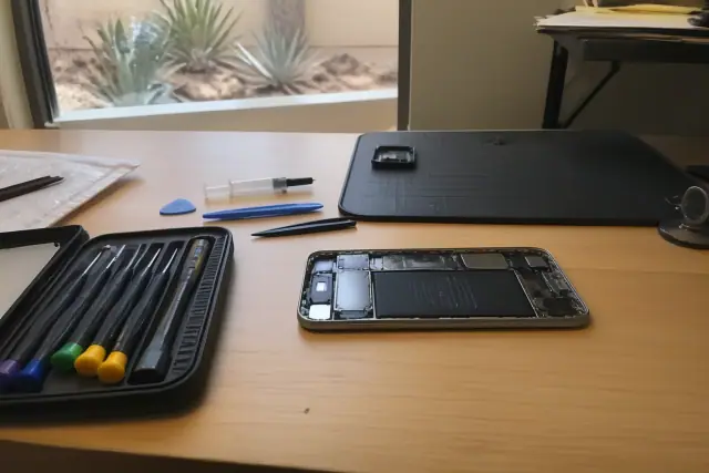 Smartphone with internal components exposed on a workstation with repair tools in Chandler, AZ.