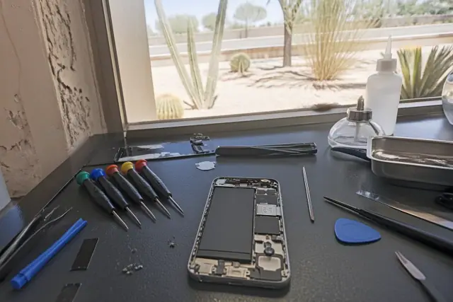 Technician repairing an opened smartphone with professional tools at a workstation in Peoria, AZ.