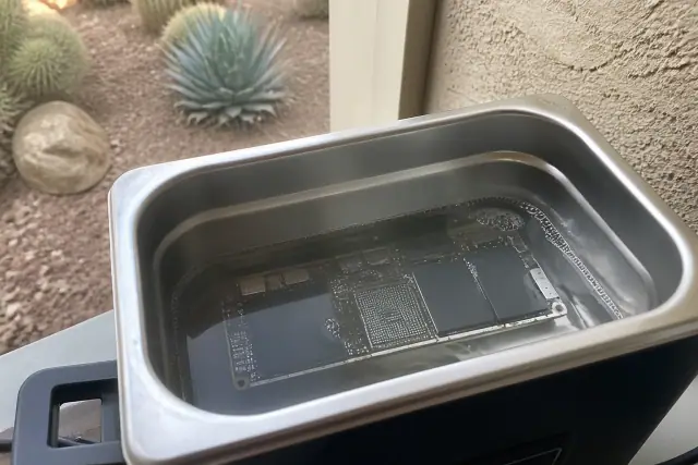 iPad circuit board submerged in an ultrasonic cleaning bath for water damage repair in Phoenix, AZ.