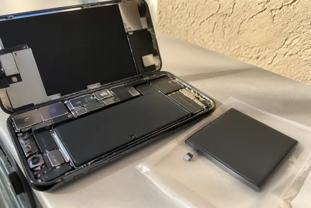 Replacement phone battery next to an open smartphone on a workshop table in Phoenix, AZ.