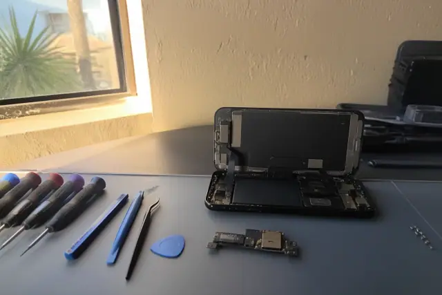 Smartphone internal components exposed during a charging port repair at a workstation in Phoenix, AZ.