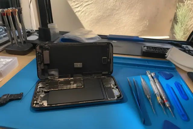 Opened smartphone with internal components exposed on a workbench with repair tools in Mesa, AZ.