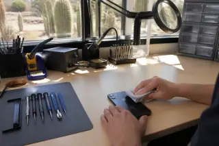 Technician cleaning a reassembled iPhone with a microfiber cloth at a sunny workbench in Phoenix, AZ.