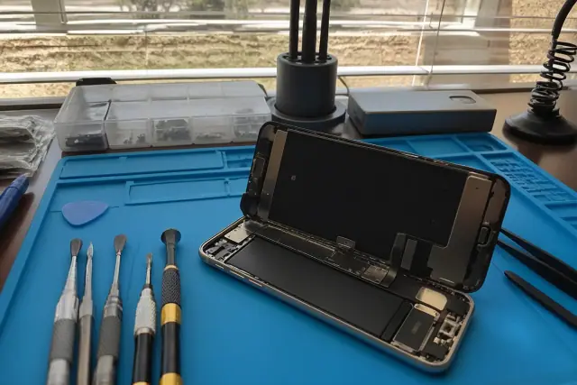 Smartphone with internal components exposed and repair tools on a workstation in Phoenix, AZ.