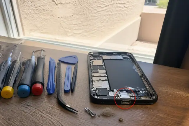 Smartphone charging port showing lint and corrosion on a workbench in Phoenix, AZ.