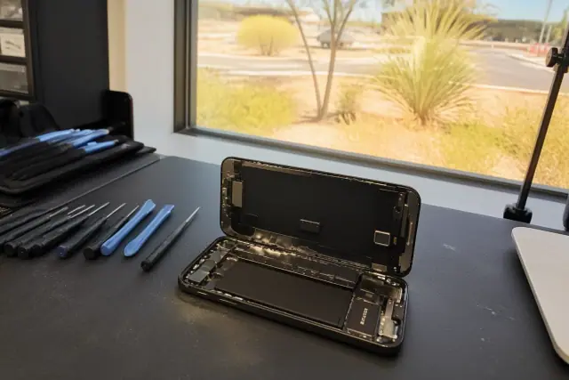 Smartphone with internal components exposed during a repair at a Phoenix, AZ workbench with desert sunlight.