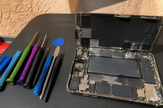 Opened smartphone with corroded logic board and repair tools on a workstation in Phoenix, AZ.