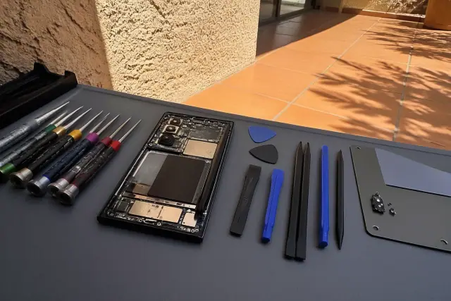 An opened smartphone with exposed internal components and repair tools on a terracotta patio in Phoenix, AZ.