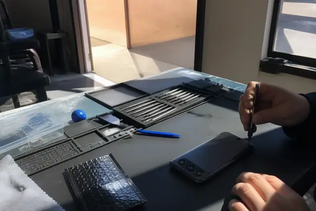 Technician using precision tools to repair a smartphone back glass at a workshop in Phoenix, AZ.