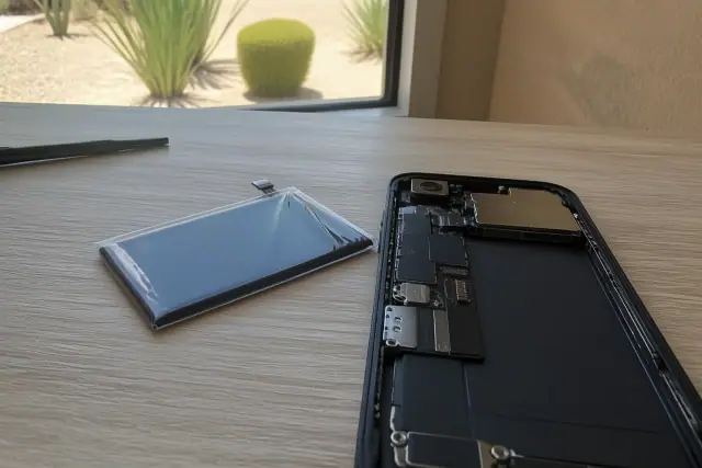 Replacement battery and open smartphone on a desk during a repair in Tempe, AZ.