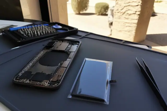 Smartphone battery replacement in progress on a workbench in Peoria, AZ.
