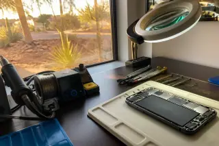 Reassembled smartphone with a new battery inside on a workbench at a Phoenix, AZ workshop during golden hour.