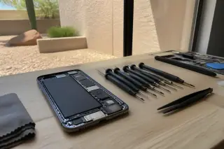 Opened smartphone chassis with a new battery and precision tools on a workbench in Phoenix, AZ.