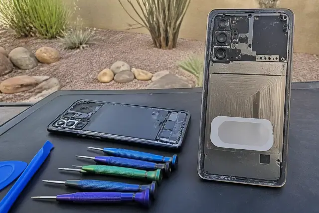 Smartphone rear chassis with internal components on a workbench in Phoenix, AZ, showing a privacy-masked IMEI area.