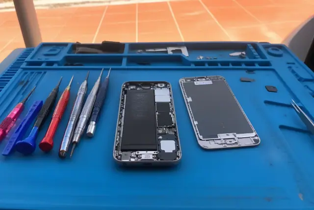 An opened smartphone with exposed internal parts and repair tools on a workbench in Phoenix, AZ.