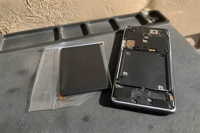 A new replacement battery next to an open smartphone on a workbench in Phoenix, AZ.