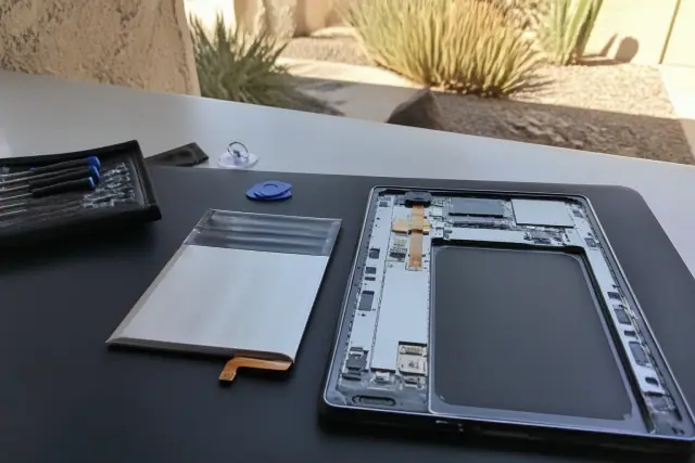 A smartphone repair technician workspace in Phoenix, AZ, showing an open phone chassis next to a new replacement battery.