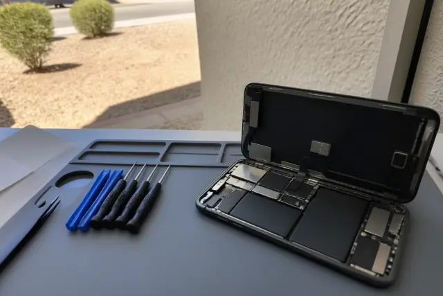An opened smartphone with internal components on a repair workstation in Mesa, AZ, with tools nearby.
