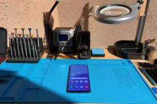 Assembled Samsung phone on a workbench with precision tools and a magnifying lamp in Phoenix, AZ.