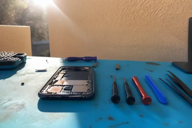 Smartphone with exposed internal components and repair tools on a workbench in Phoenix, AZ.