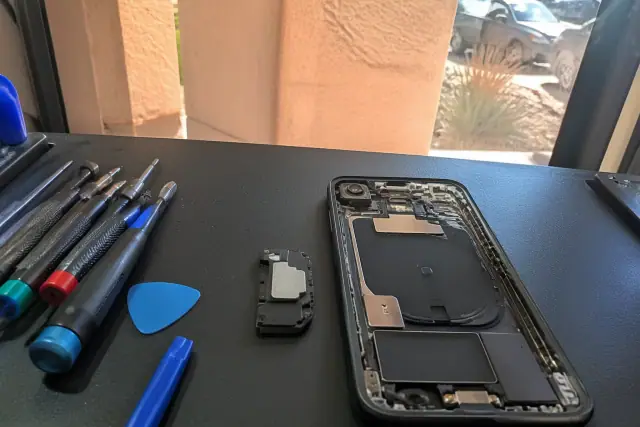 Open smartphone with exposed internal speaker and repair tools on a workbench in Phoenix, AZ.