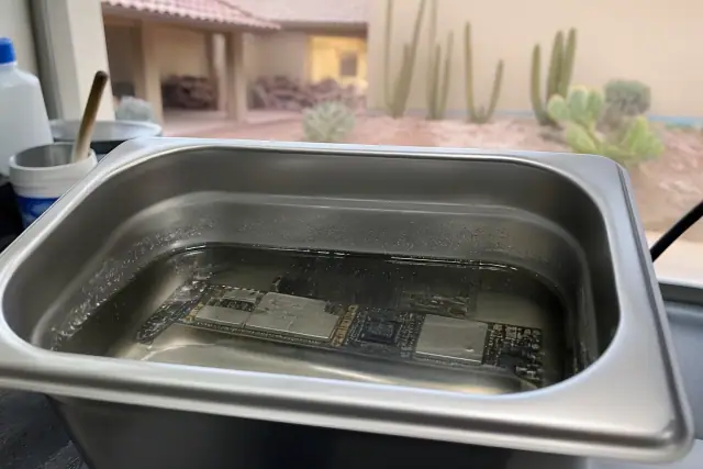 Smartphone logic board submerged in an ultrasonic cleaning tank to remove corrosion at a workshop in Glendale, AZ.