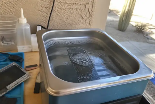 A circuit board in an ultrasonic cleaning bath for phone water damage repair at a workbench in Tempe, AZ.