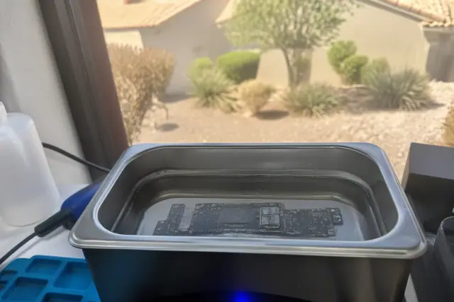 Smartphone circuit board submerged in an ultrasonic cleaning solution during a repair in Peoria, AZ.