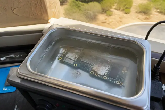 Smartphone circuit board submerged in an ultrasonic cleaner for water damage repair in Scottsdale, AZ.