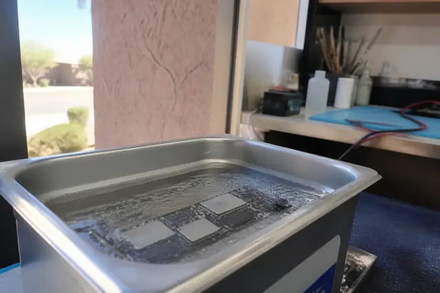 Smartphone circuit board submerged in an ultrasonic cleaner for water damage repair in a workshop in Gilbert, AZ.