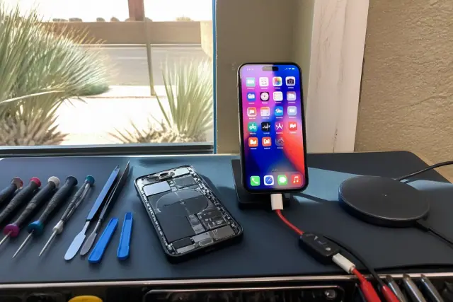 Smartphone with exposed internal components undergoing wired and wireless charging tests at a workshop in Phoenix, AZ.