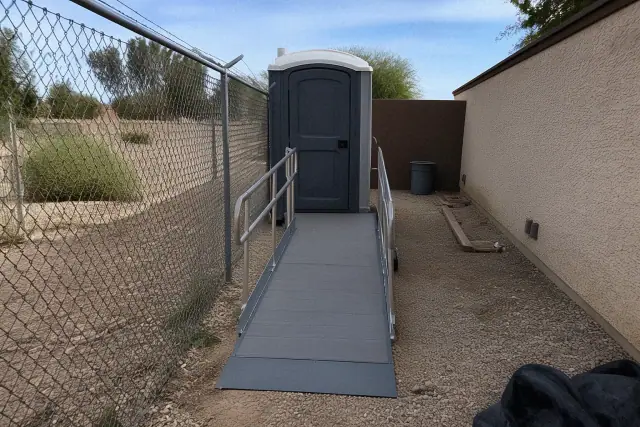 ADA-compliant portable toilet with ramp access on a gravel maintenance path in Phoenix, AZ.