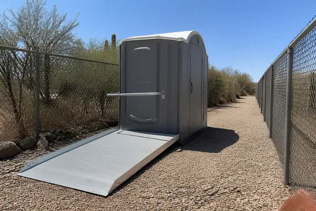 ADA-compliant portable toilet with a metal access ramp on a gravel worksite in Peoria, AZ.