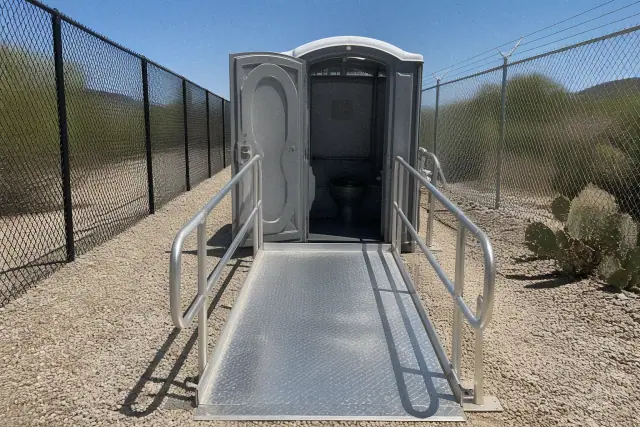 ADA-compliant portable toilet with an aluminum access ramp on a gravel site in Glendale, AZ.